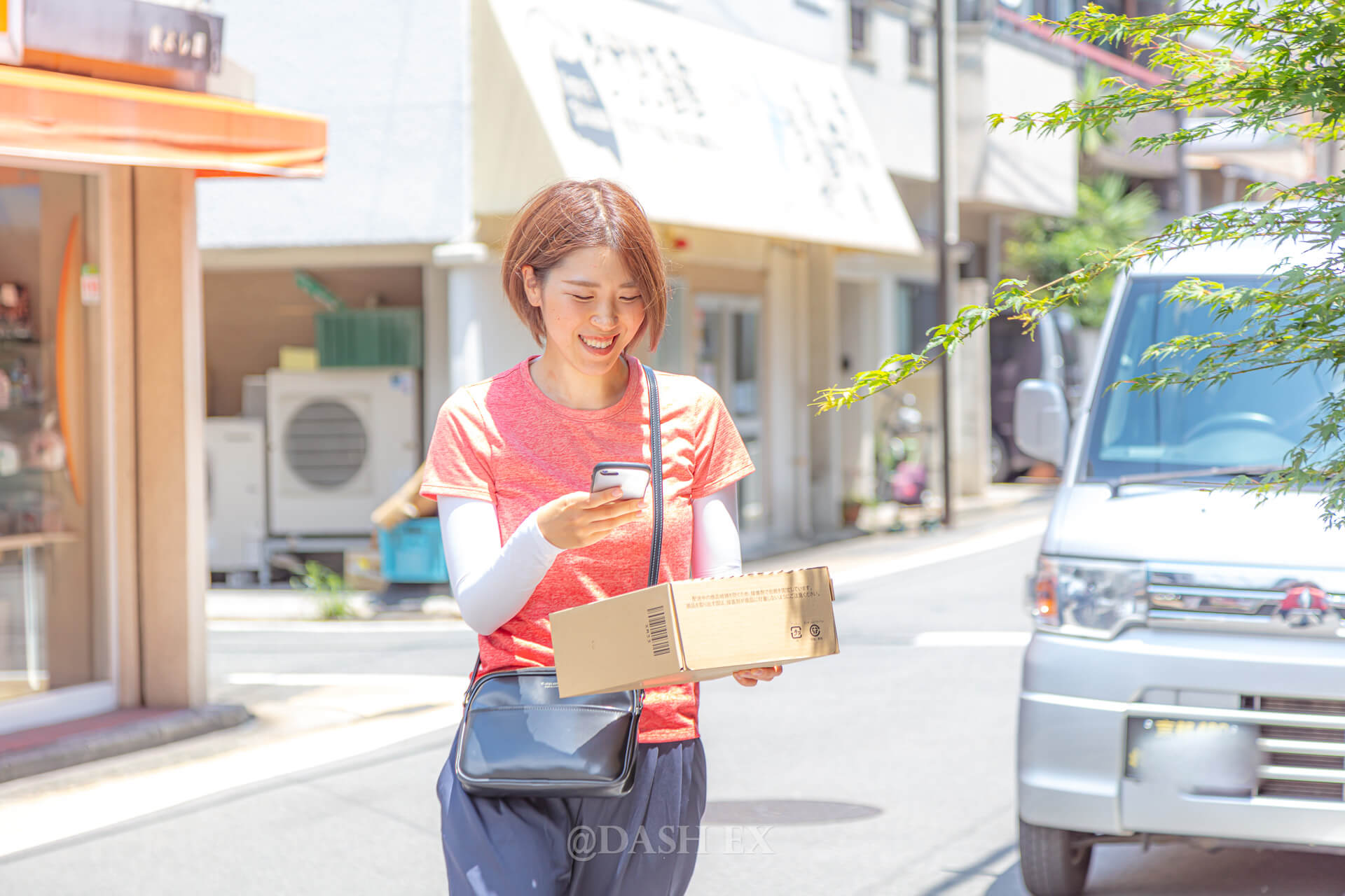 荷物を抱えてスマートフォンを確認する女性と軽バン